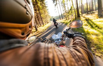 Man seat on the motorcycle on the forest road during sunrise.