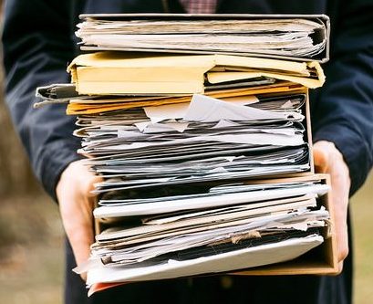 Torso and hands of a person holding a large stack of manila folders