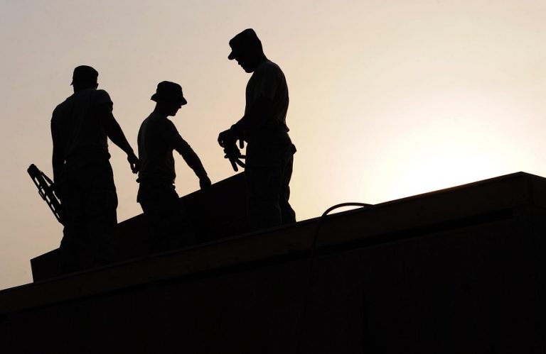 Three construction workers on a roof silhouetted by the setting sun