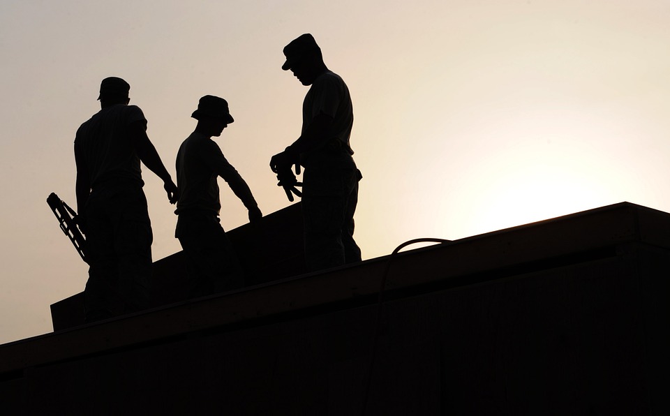 Three construction workers on a roof silhouetted by the setting sun