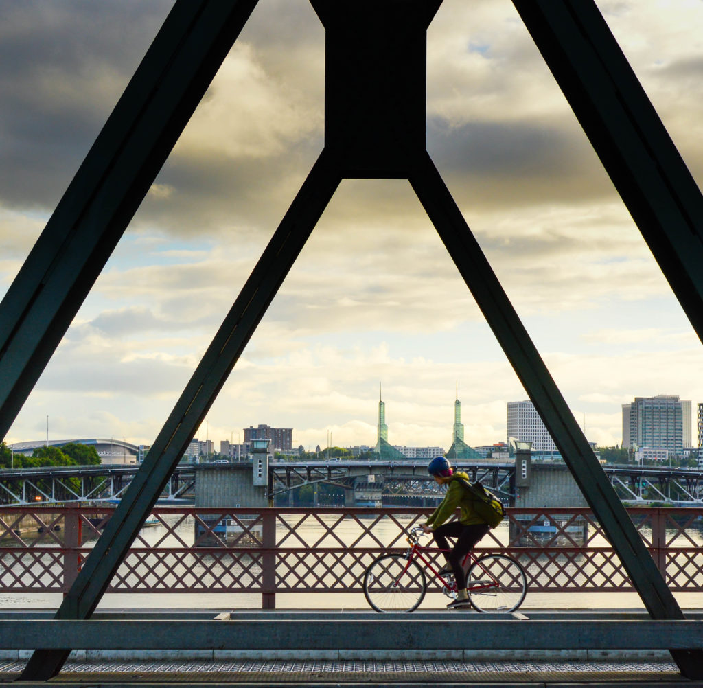 A picture of a biker crossing a bridge in Portland with a cloudy sky in the background.