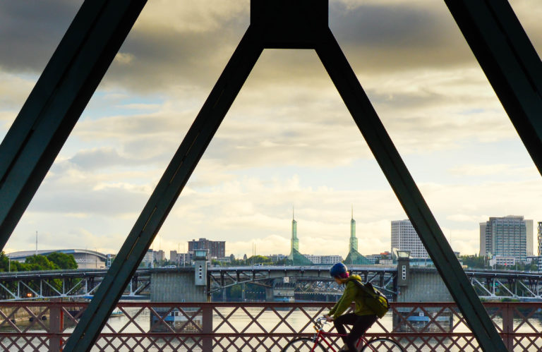 A picture of a biker crossing a bridge in Portland with a cloudy sky in the background.