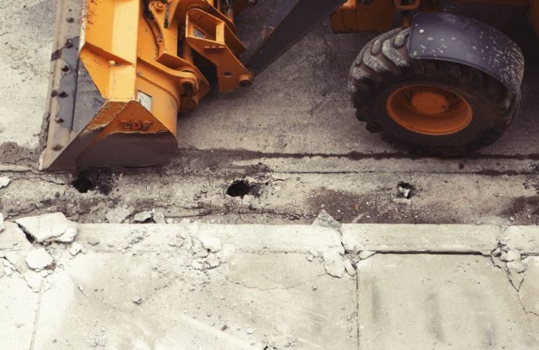 Construction equipment moving beside a damaged concrete sidewalk. Closures of sidewalks and bike lanes for construction are dangerous and often avoidable, and the state of Oregon could be doing more to protect non-motorized road users.