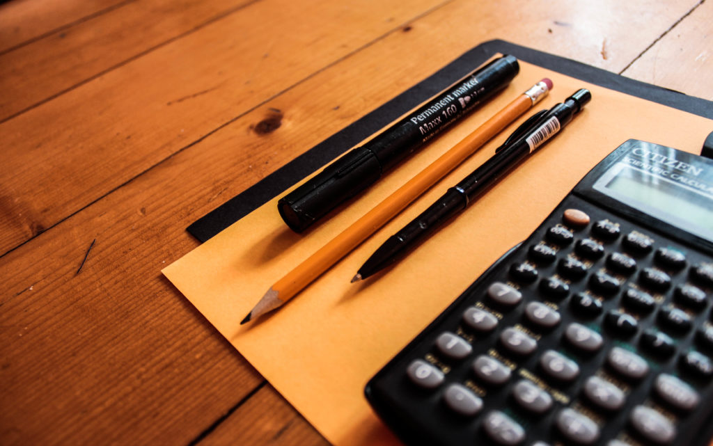 A calculator, pencil, and pens sitting on a desk