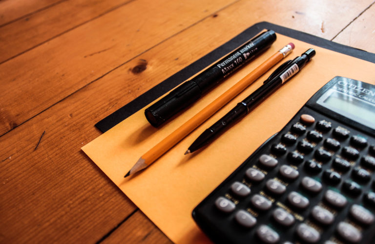 A calculator, pencil, and pens sitting on a desk