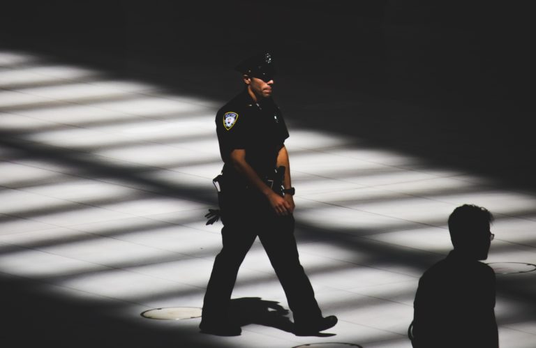 A policeman walking through slats of sunlight