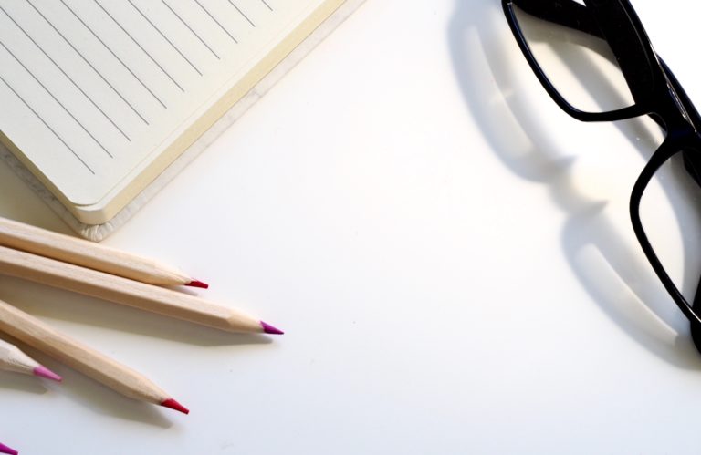 A picture of a notepad, glasses, and pencils